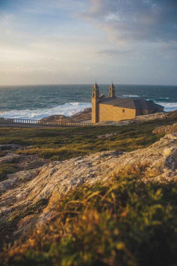 Coastal view of a stone church with twin towers overlooking the ocean and rocky landscape.